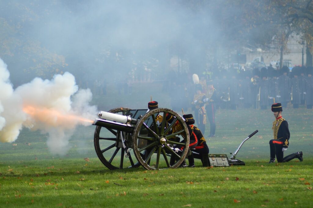 group of men firing canyon on green field surrounded with people watching