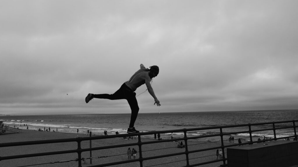 man standing on metal railing overlooking beach shoreline under gray cloudy skies at daytime