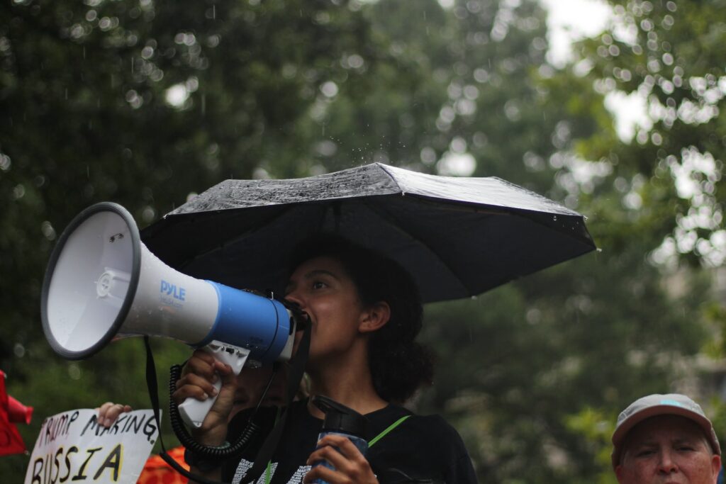 woman standing holding umbrella and white megaphone during daytime