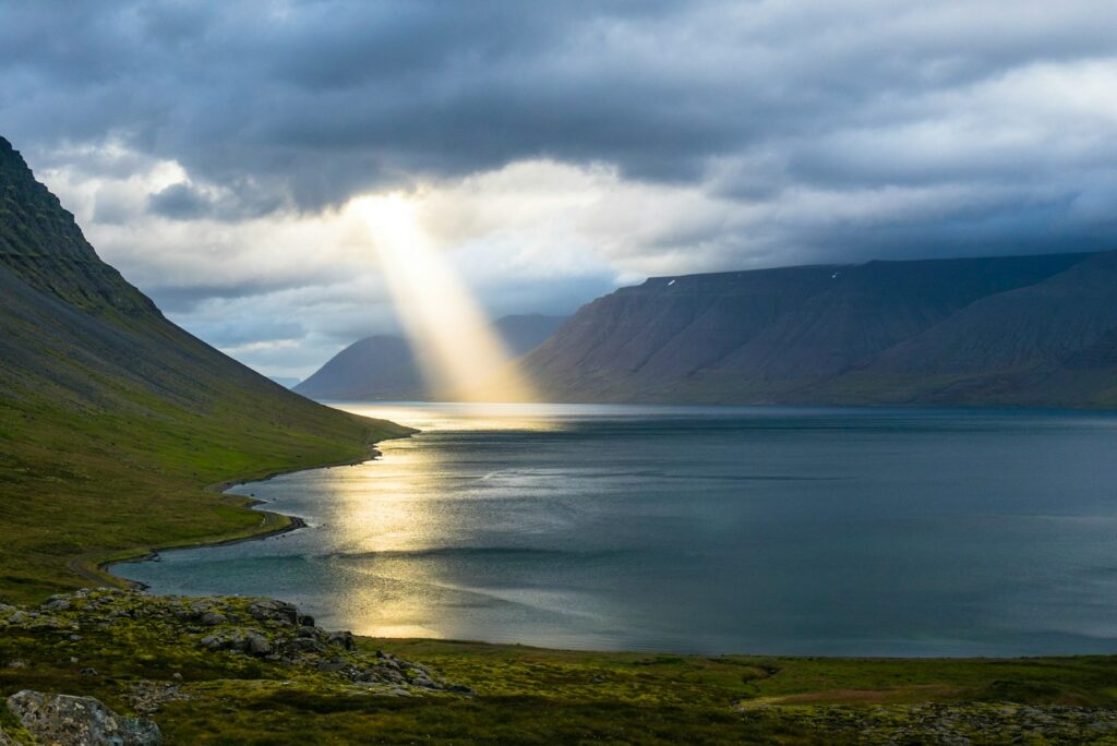 sun reflection on calm water near green mountains