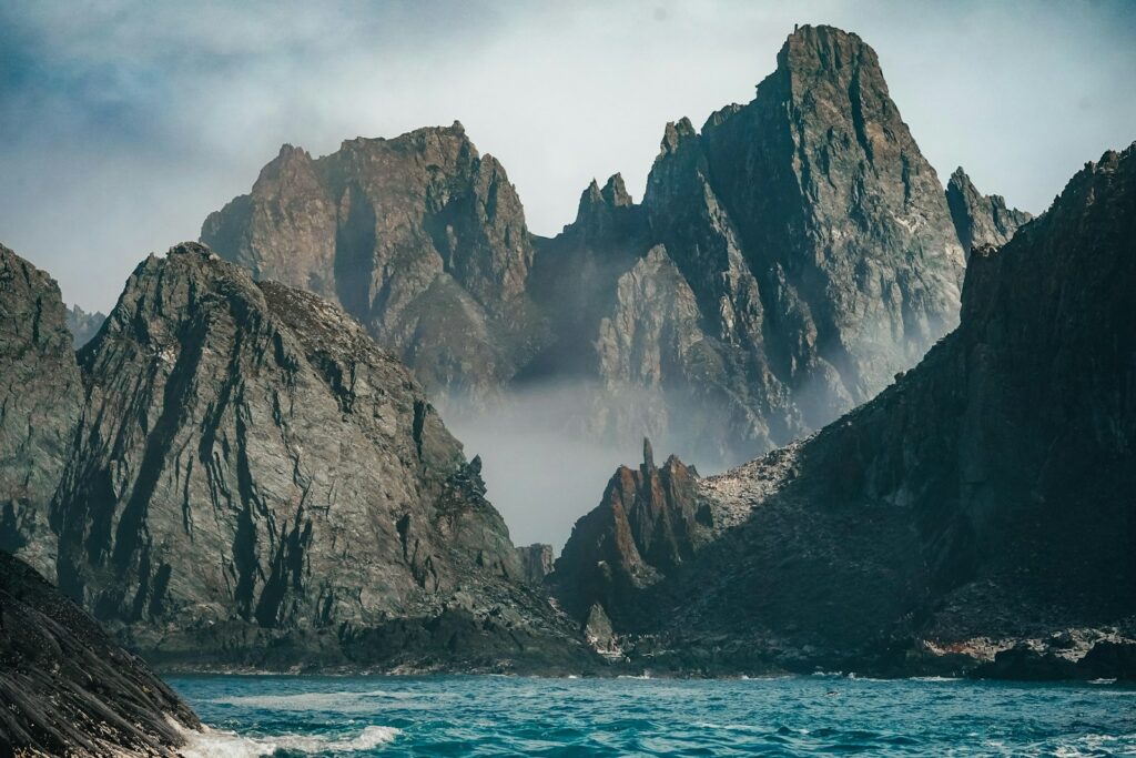 brown rocky mountain beside blue sea under white sky during daytime