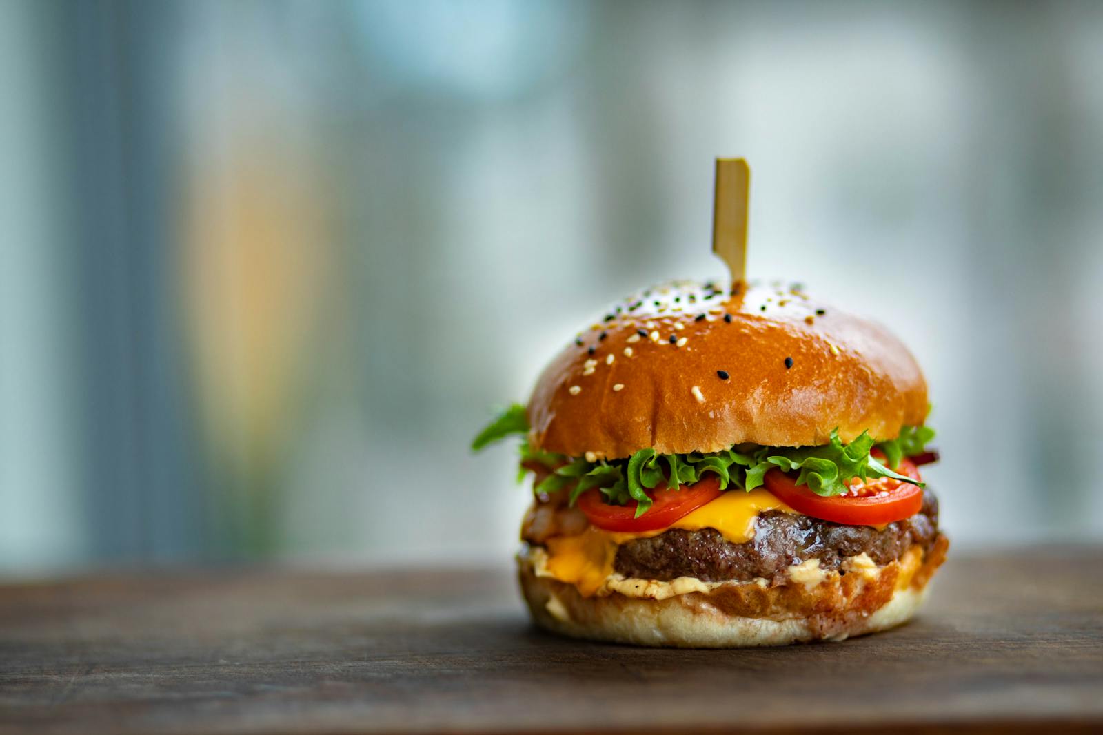 Mouthwatering cheeseburger with fresh tomatoes and lettuce on a wooden surface.